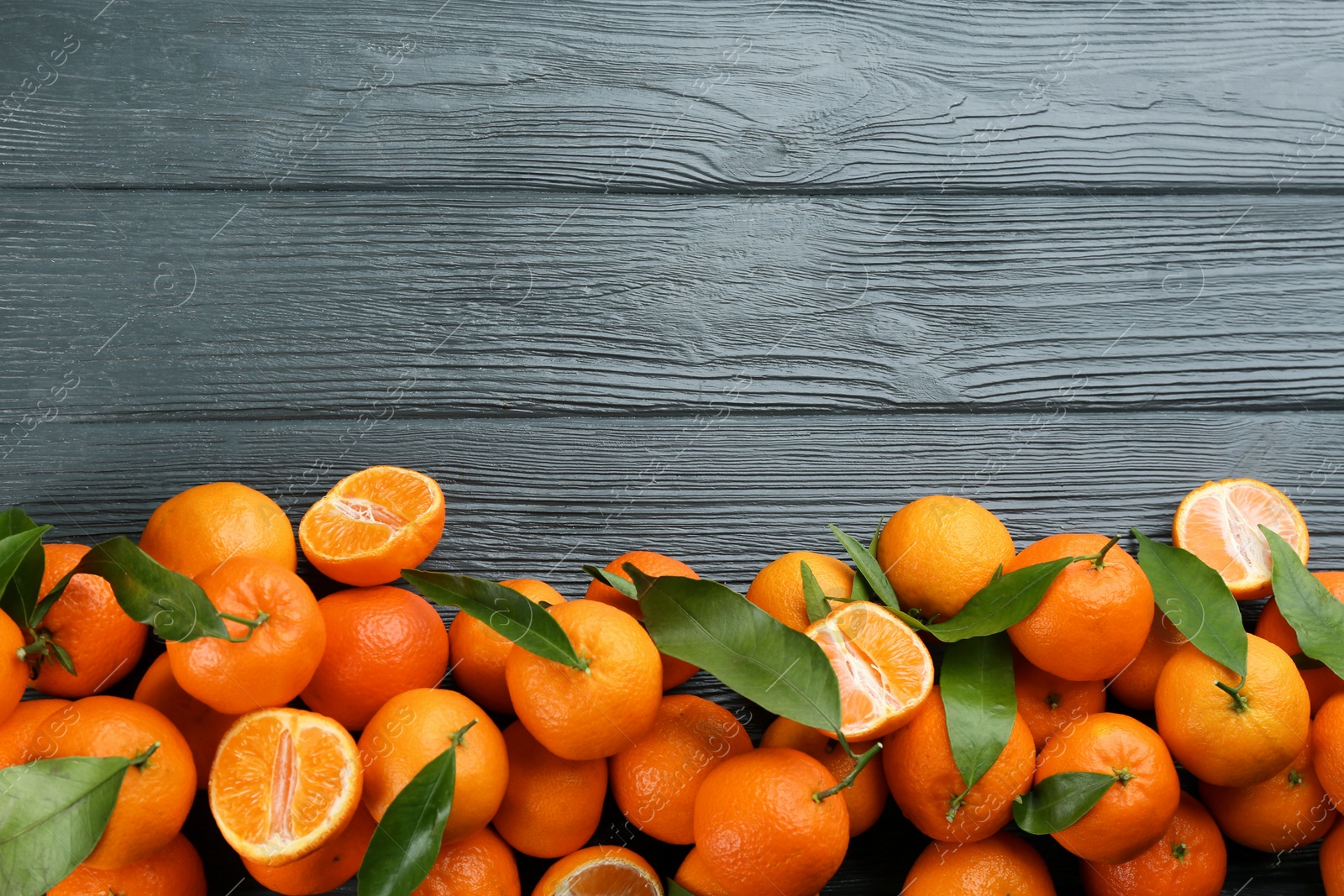 Photo of Fresh tangerines with green leaves on grey wooden table, flat lay. Space for text