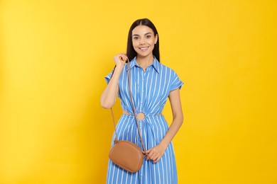 Beautiful young woman with stylish bag on orange background