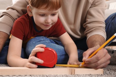 Photo of Father and son measuring plank indoors, closeup. Repair work