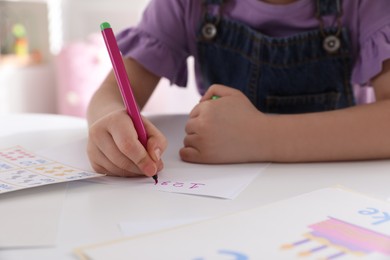Photo of Little girl writing numbers in classroom at English lesson, closeup