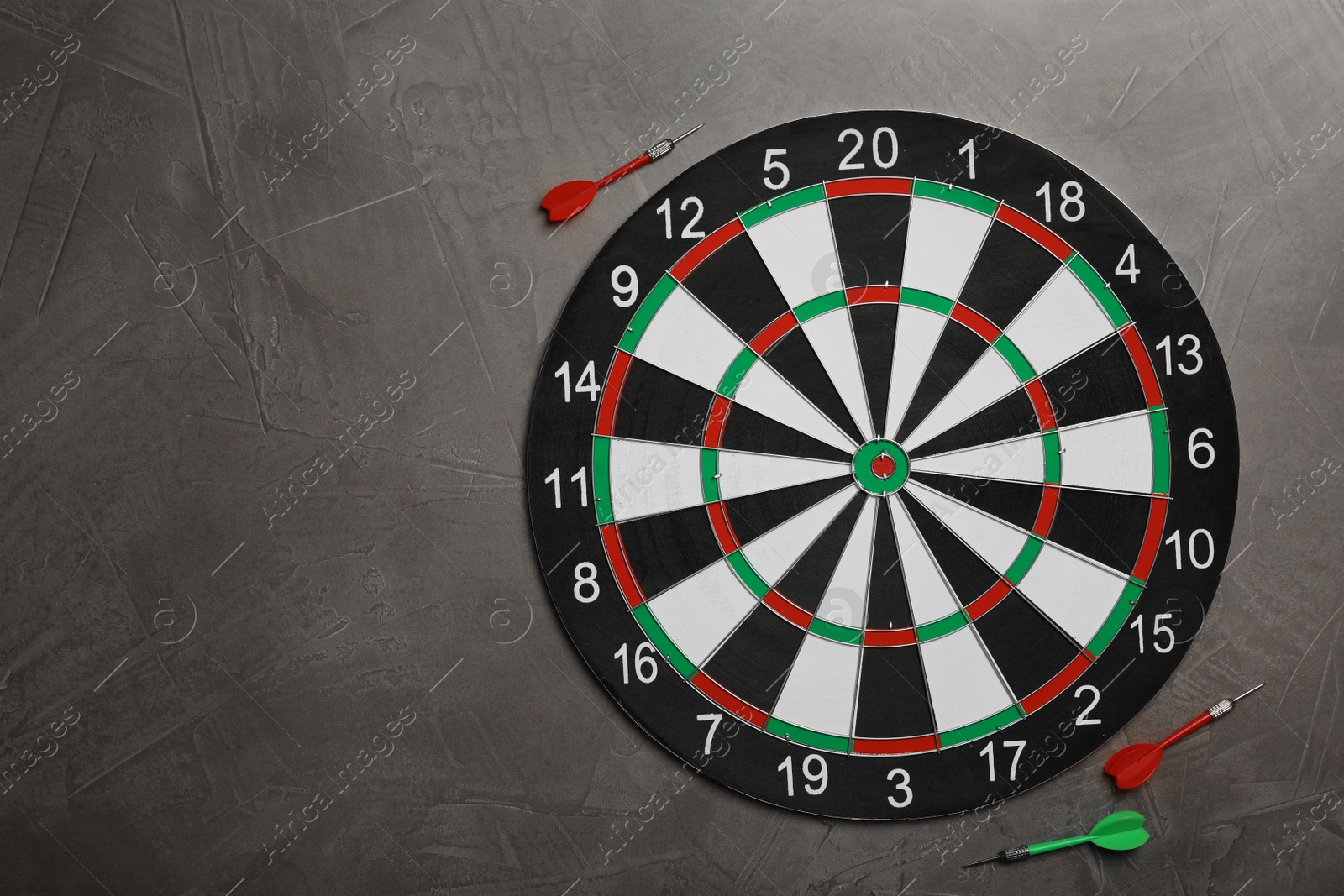 Photo of Dart board with color arrows on grey stone background, top view. Space for text