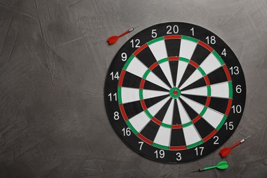 Photo of Dart board with color arrows on grey stone background, top view. Space for text