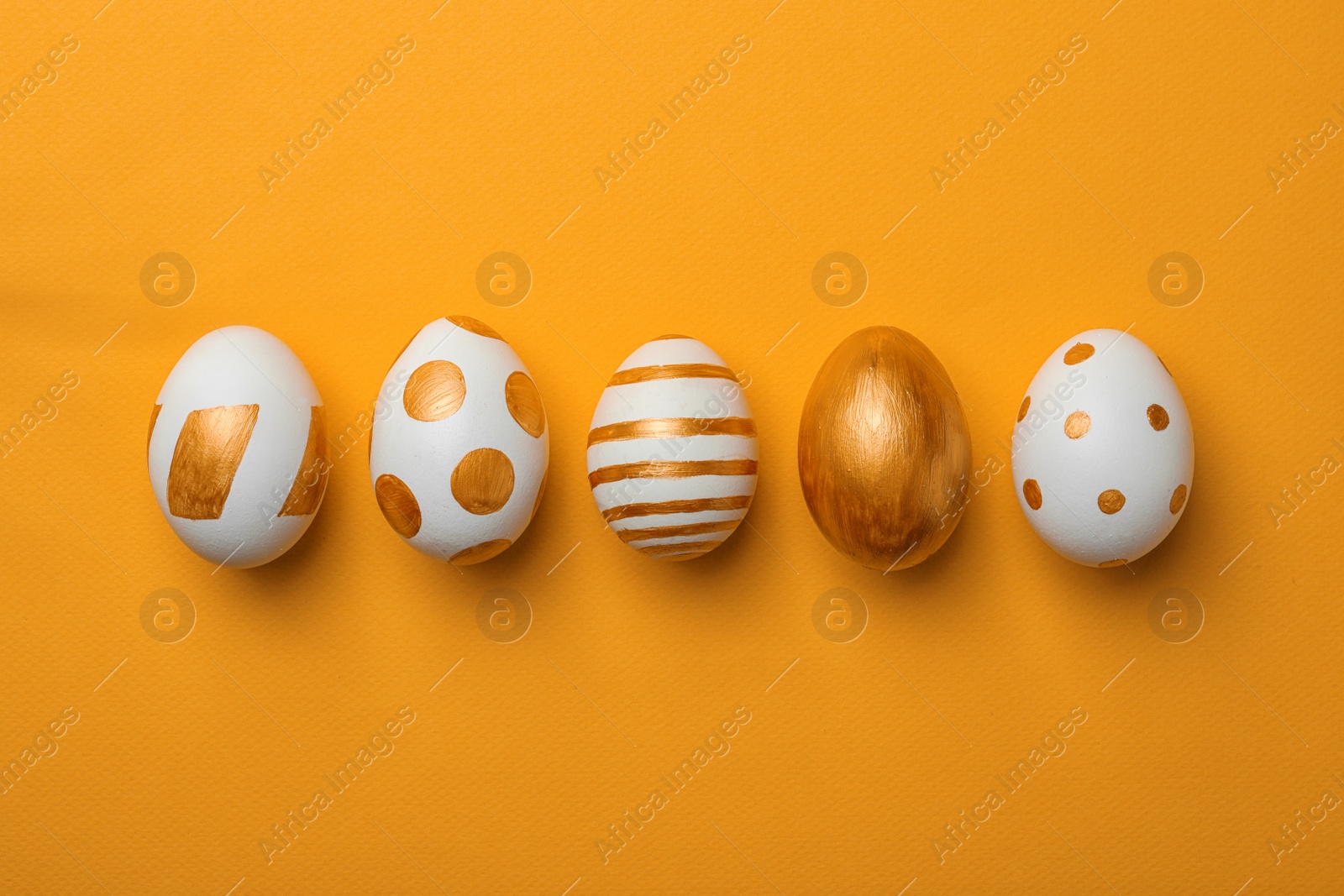 Photo of Set of traditional Easter eggs decorated with golden paint on color background, top view