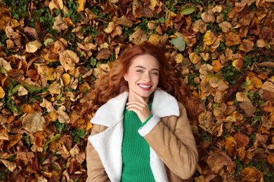 Photo of Smiling woman lying among autumn leaves outdoors, top view