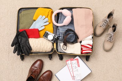 Photo of Open suitcase with warm clothes, accessories and shoes on floor, flat lay