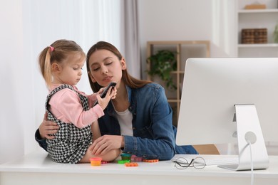 Photo of Mother spending time with her daughter at home. Child sitting on desk. Taking break in remote work