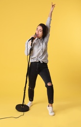 Young woman wearing casual clothes singing in microphone on color background