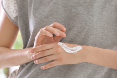 Photo of Young woman applying cream on her hands, closeup