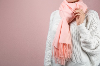 Woman wearing warm scarf on pink background, closeup with space for text. Autumn clothes