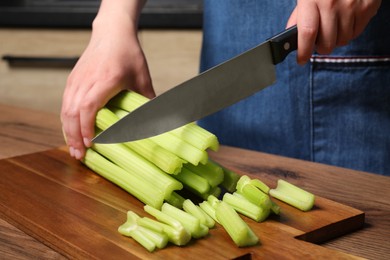 Woman cutting fresh green celery at wooden table, closeup