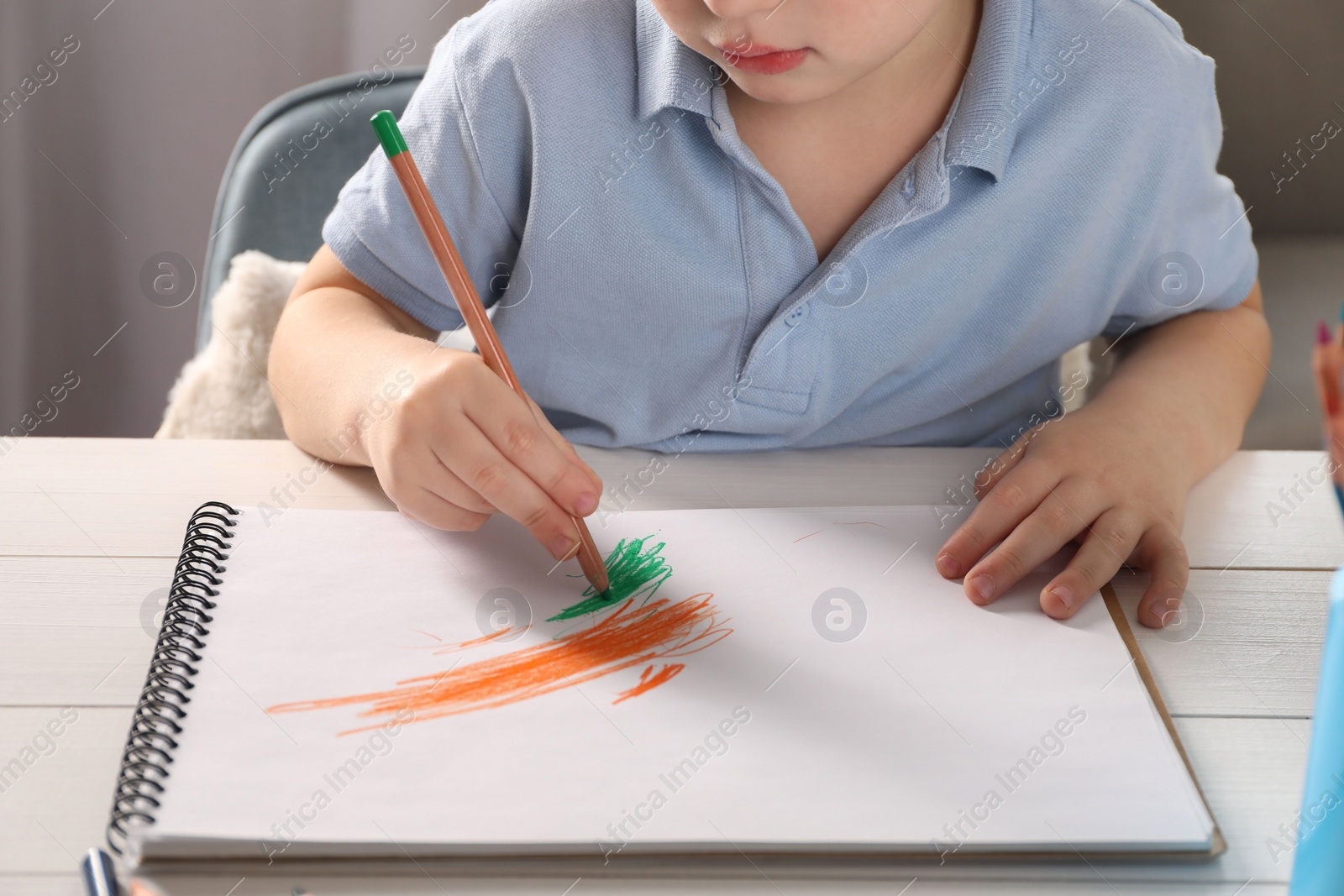 Photo of Little boy drawing with pencil at white wooden table, closeup. Child`s art