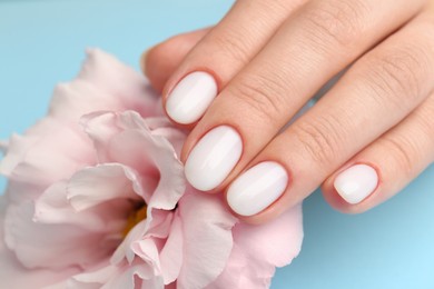 Photo of Woman with white nail polish touching pink eustoma flower on light blue background, closeup