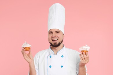 Photo of Happy professional confectioner in uniform holding delicious cupcakes on pink background