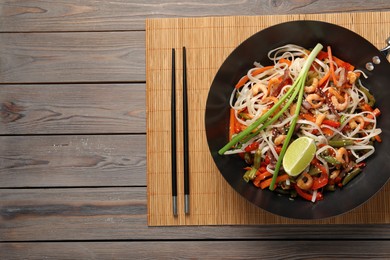 Shrimp stir fry with noodles and vegetables in wok on wooden table, top view. Space for text