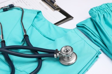 Photo of Medical uniform, stethoscope and clipboard on white background