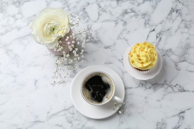 Photo of Delicious cupcake with yellow cream, coffee and flowers on white marble table, flat lay
