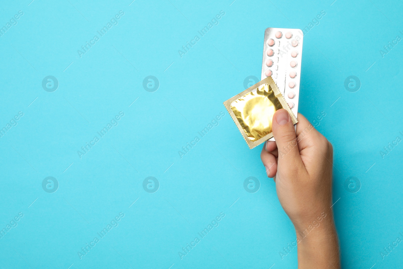 Photo of Woman holding condom and birth control pills on blue background, top view with space for text. Safe sex