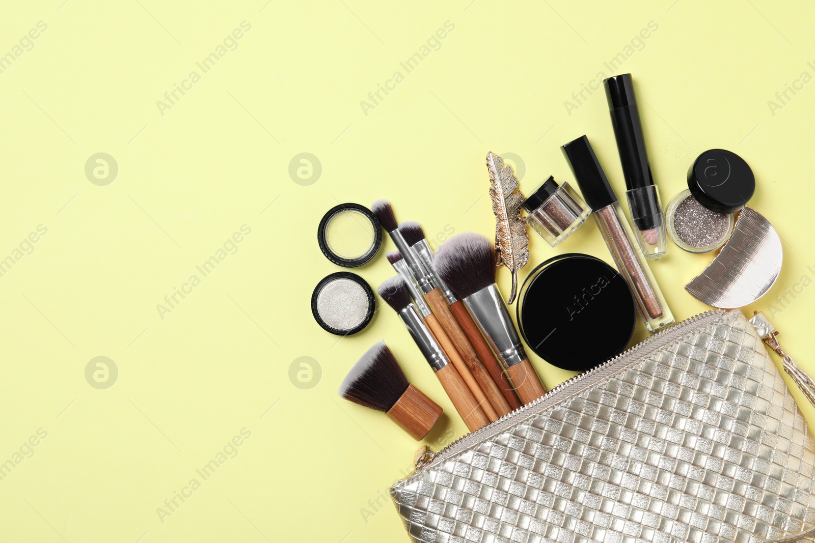 Photo of Cosmetic bag with makeup products and beauty accessories on yellow background, flat lay. Space for text