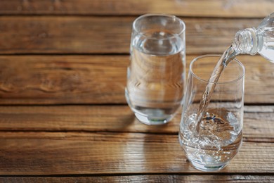 Photo of Pouring water from bottle into glass on wooden table, space for text