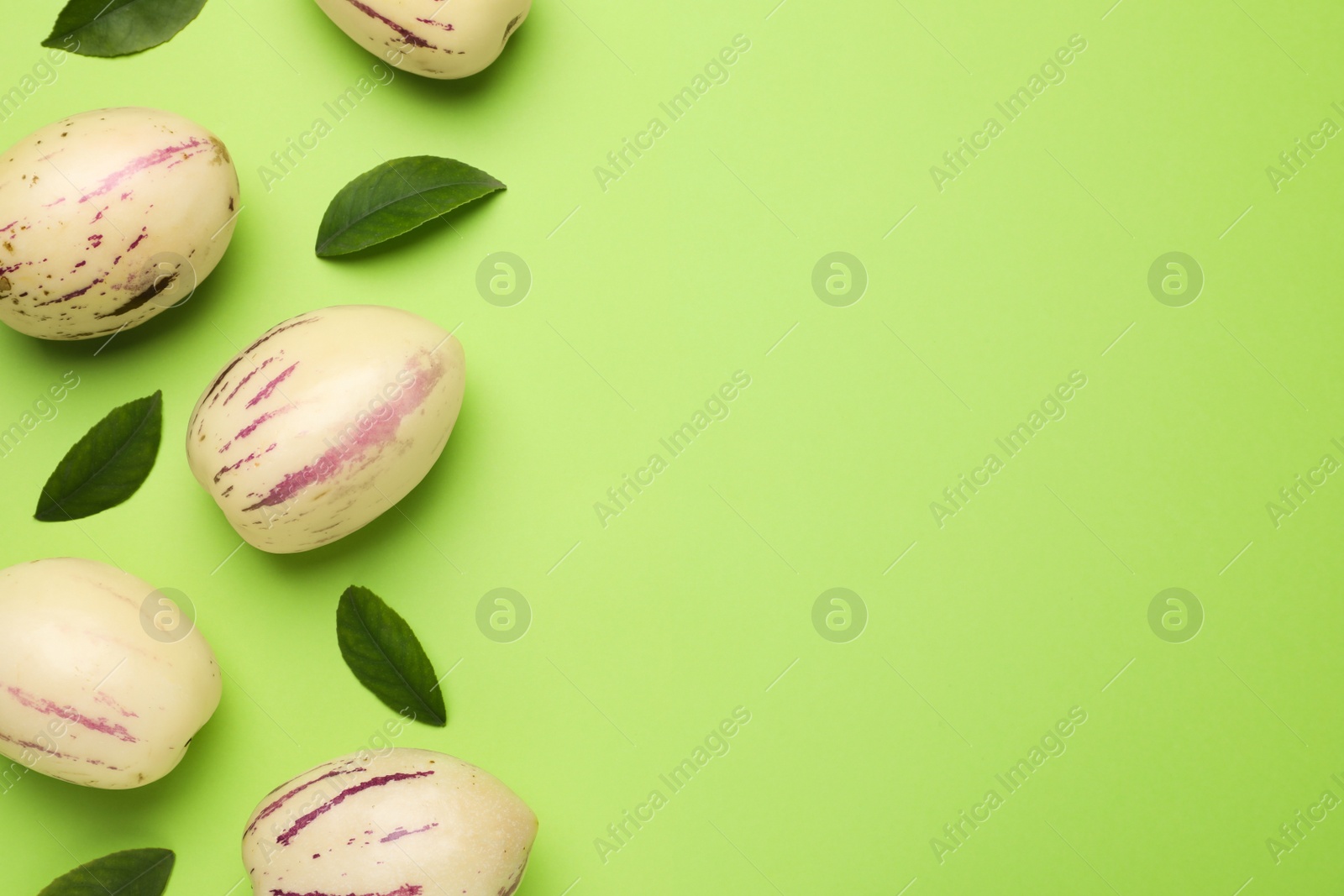Photo of Fresh ripe pepino melons and leaves on green background, flat lay. Space for text