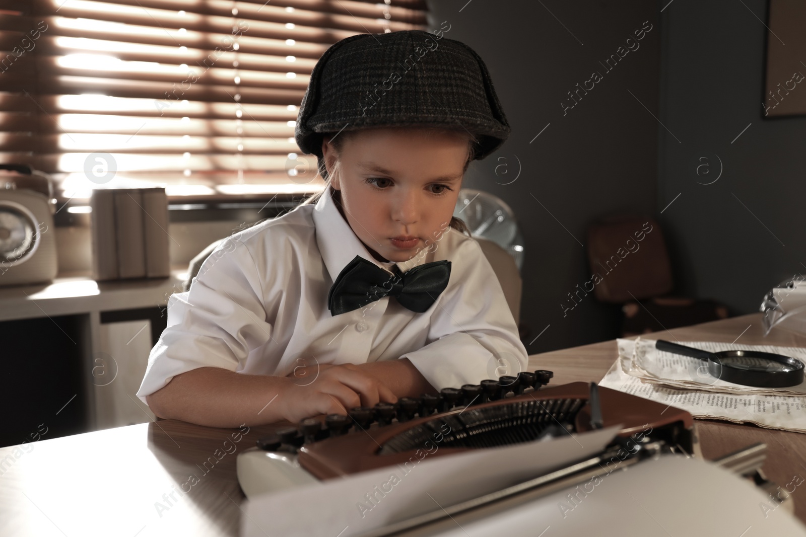 Photo of Cute little detective using typewriter at table in office