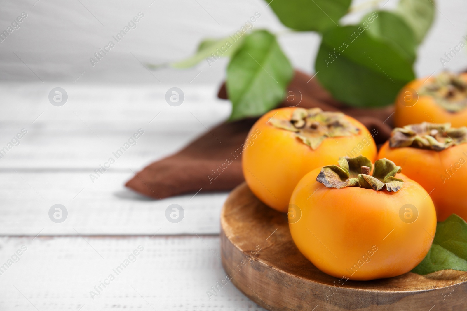Photo of Delicious ripe juicy persimmons on white wooden table, closeup. Space for text