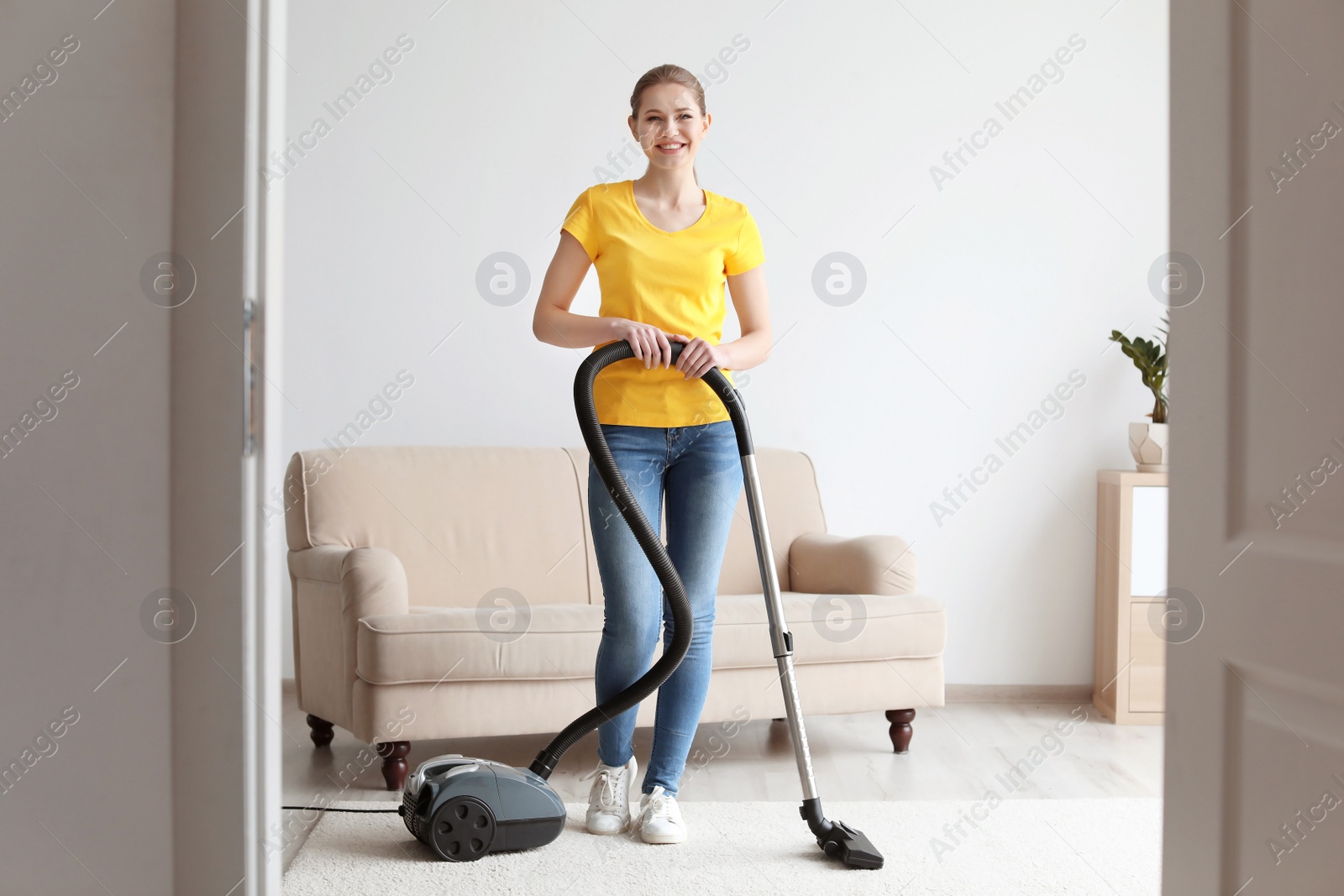 Photo of Young woman cleaning carpet with vacuum in living room