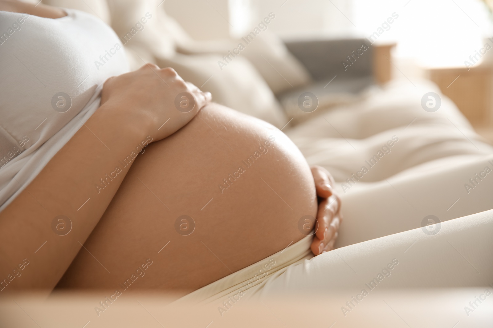 Photo of Pregnant woman touching her belly indoors, closeup