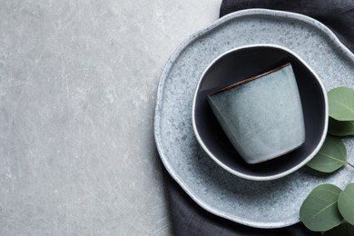 Set of dishware with eucalyptus leaves and napkin on grey table, flat lay. Space for text