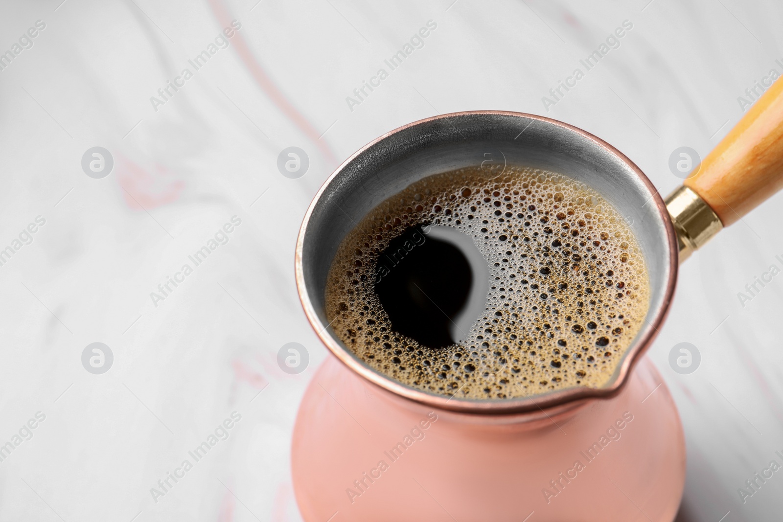 Photo of Turkish coffee in cezve on white marble table, closeup. Space for text