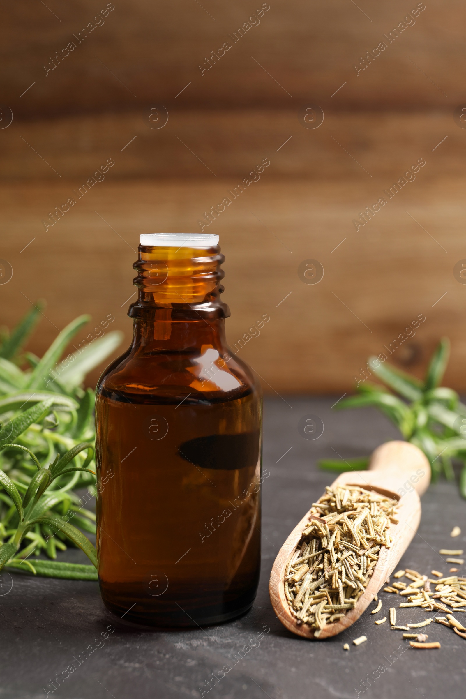 Photo of Bottle of essential oil, fresh and dry rosemary on gray table