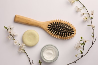 Photo of Wooden hairbrush, cosmetic products and branch with flowers on white background, flat lay