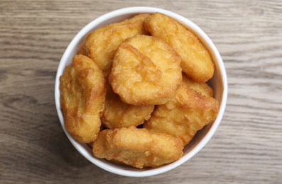 Photo of Bucket with tasty chicken nuggets on wooden table, top view