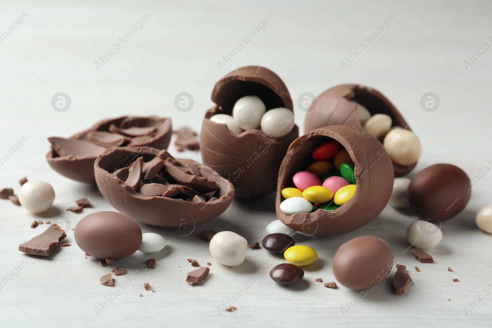 Photo of Broken chocolate eggs with candies on white wooden table