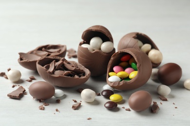 Photo of Broken chocolate eggs with candies on white wooden table