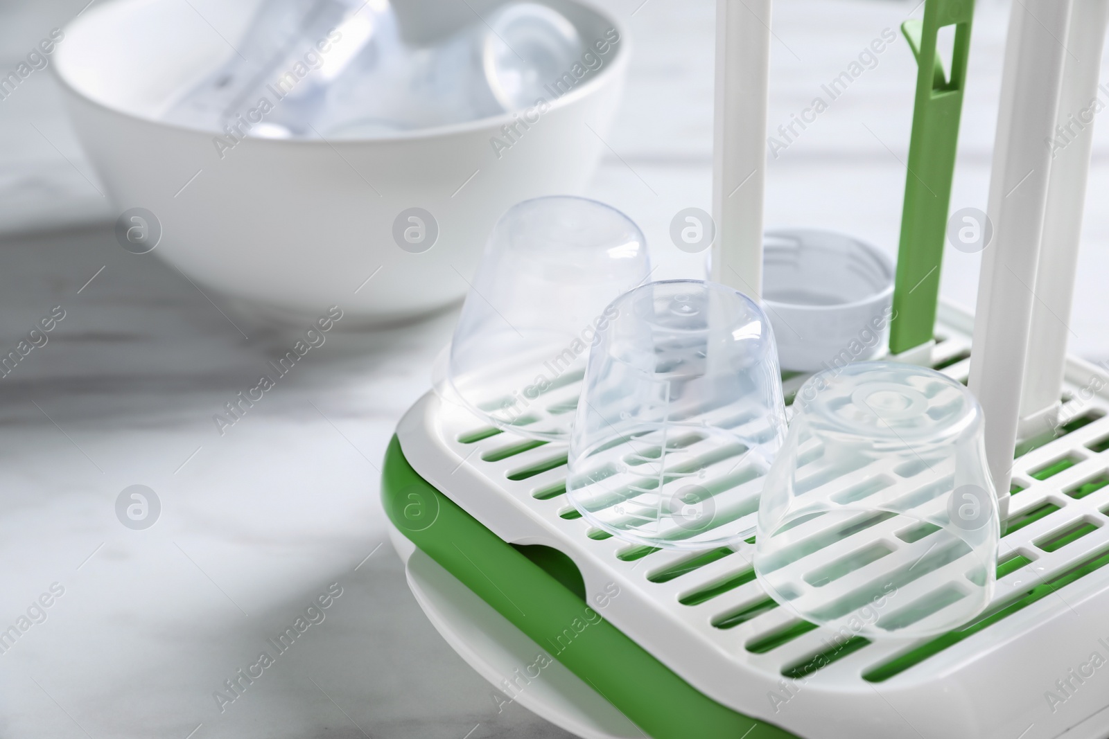 Photo of Dryer with baby bottle caps on white marble table in kitchen, closeup. Space for text