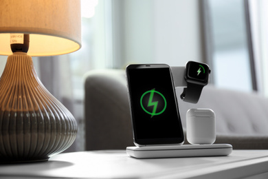 Photo of Smartphone, watch and earphones charging on wireless pad in room