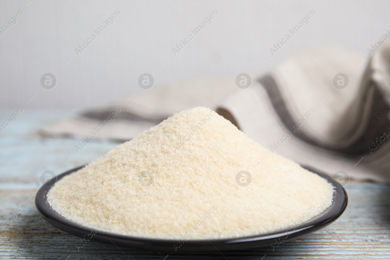 Photo of Plate with gelatin powder on light blue wooden table. Space for text