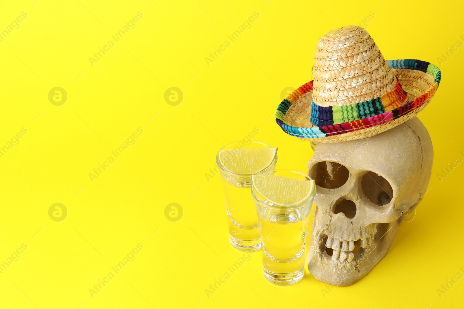 Photo of Human scull with Mexican sombrero hat, tequila in glasses and lime on yellow background, space for text