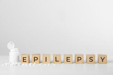 Photo of Wooden cubes with word Epilepsy and pills on white table, space for text