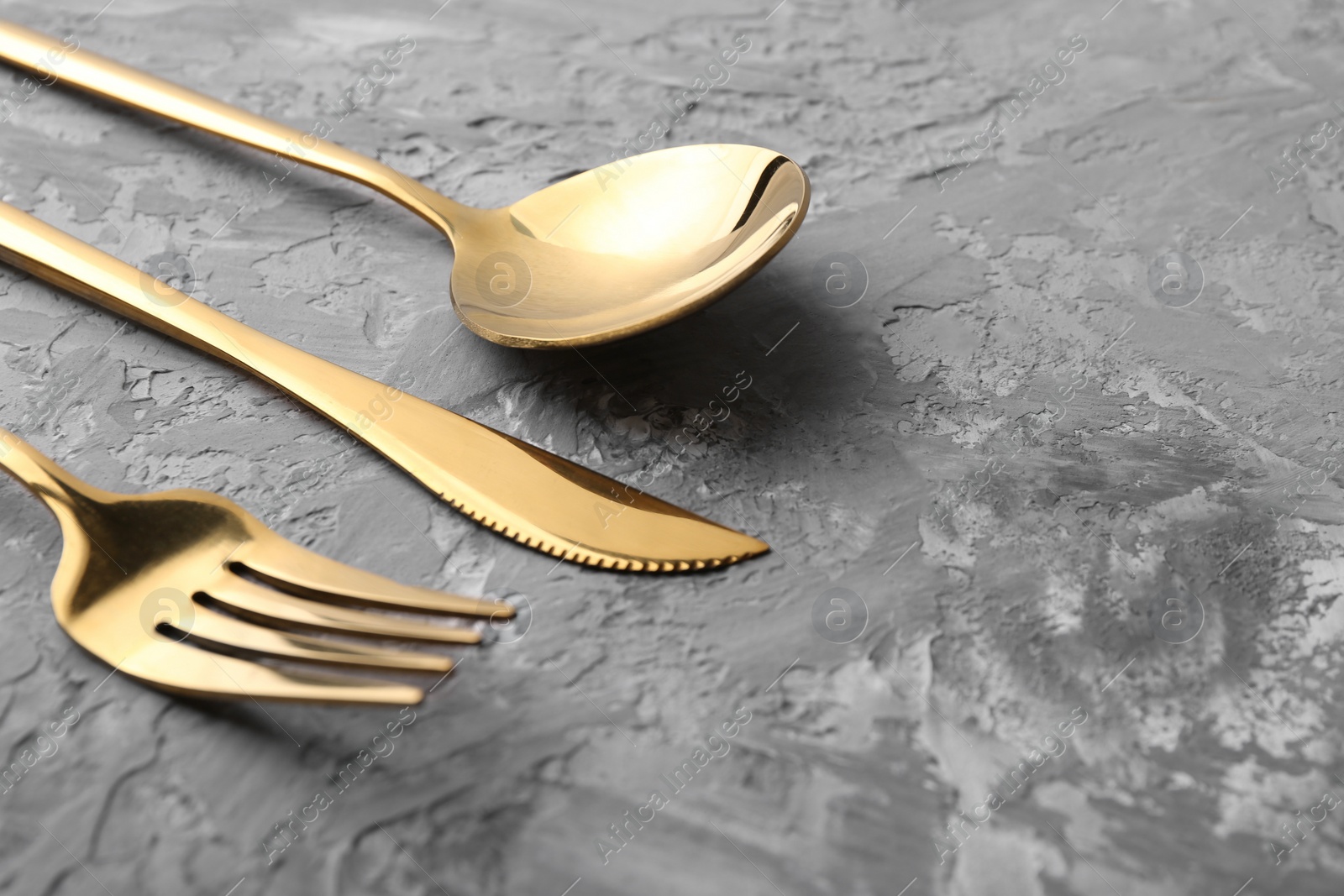 Photo of Stylish golden cutlery set on grey textured table, closeup. Space for text