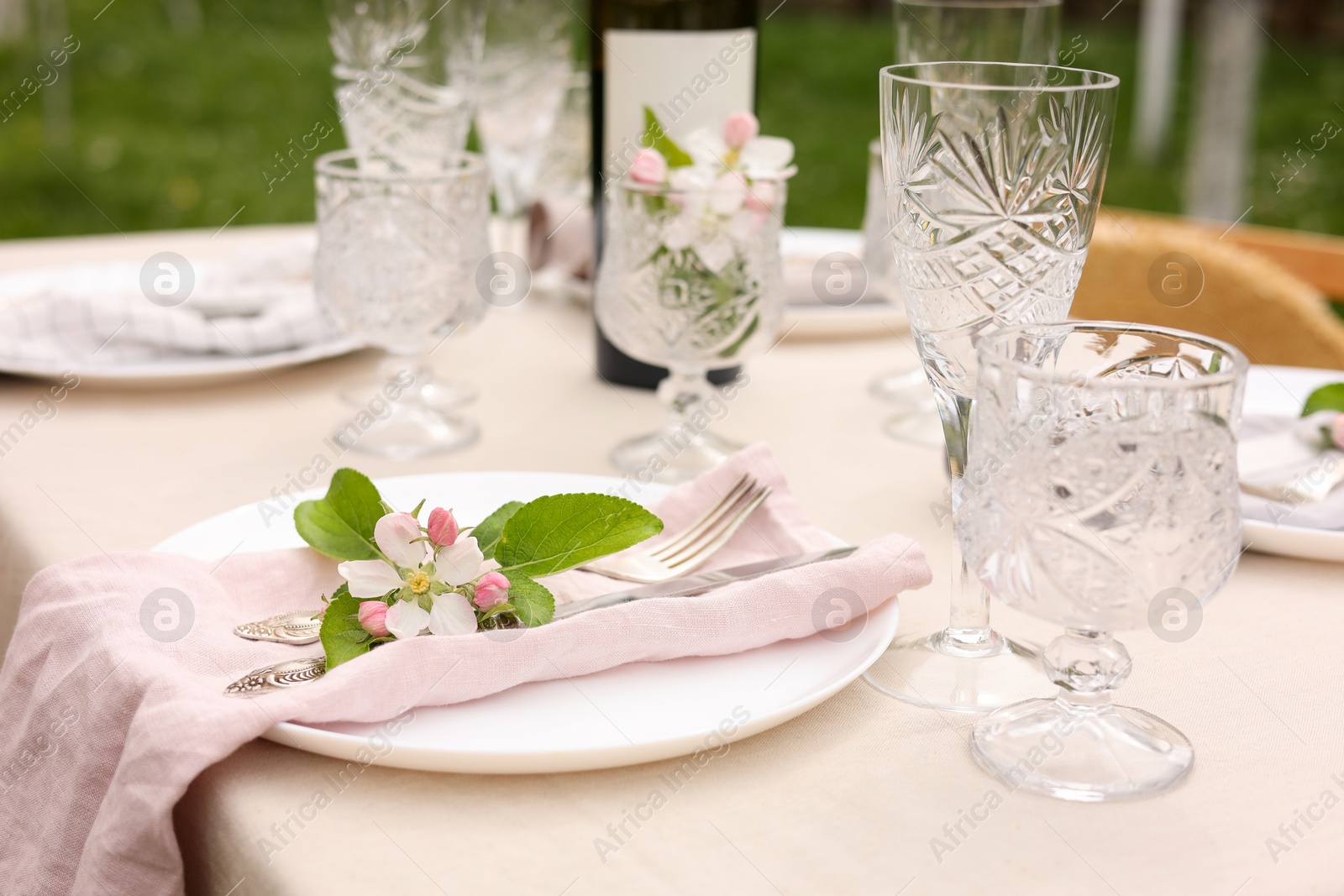 Photo of Stylish table setting with beautiful spring flowers, wine, plates and glasses in garden