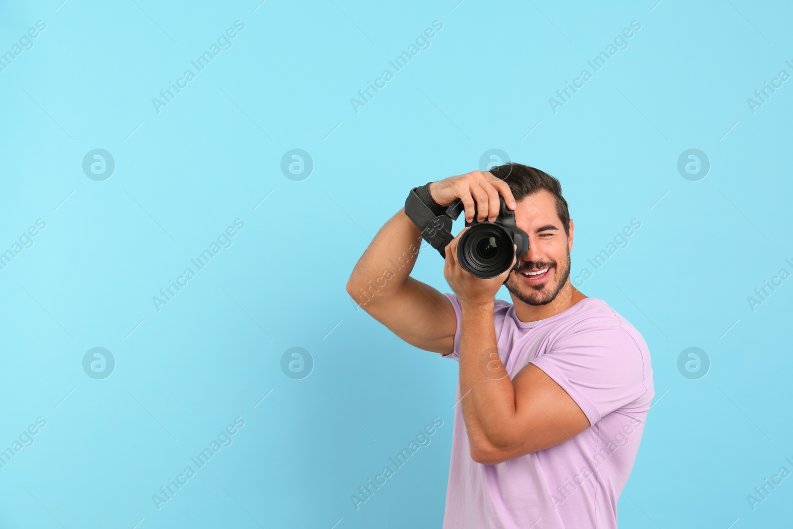 Photo of Young professional photographer taking picture on light blue background. Space for text