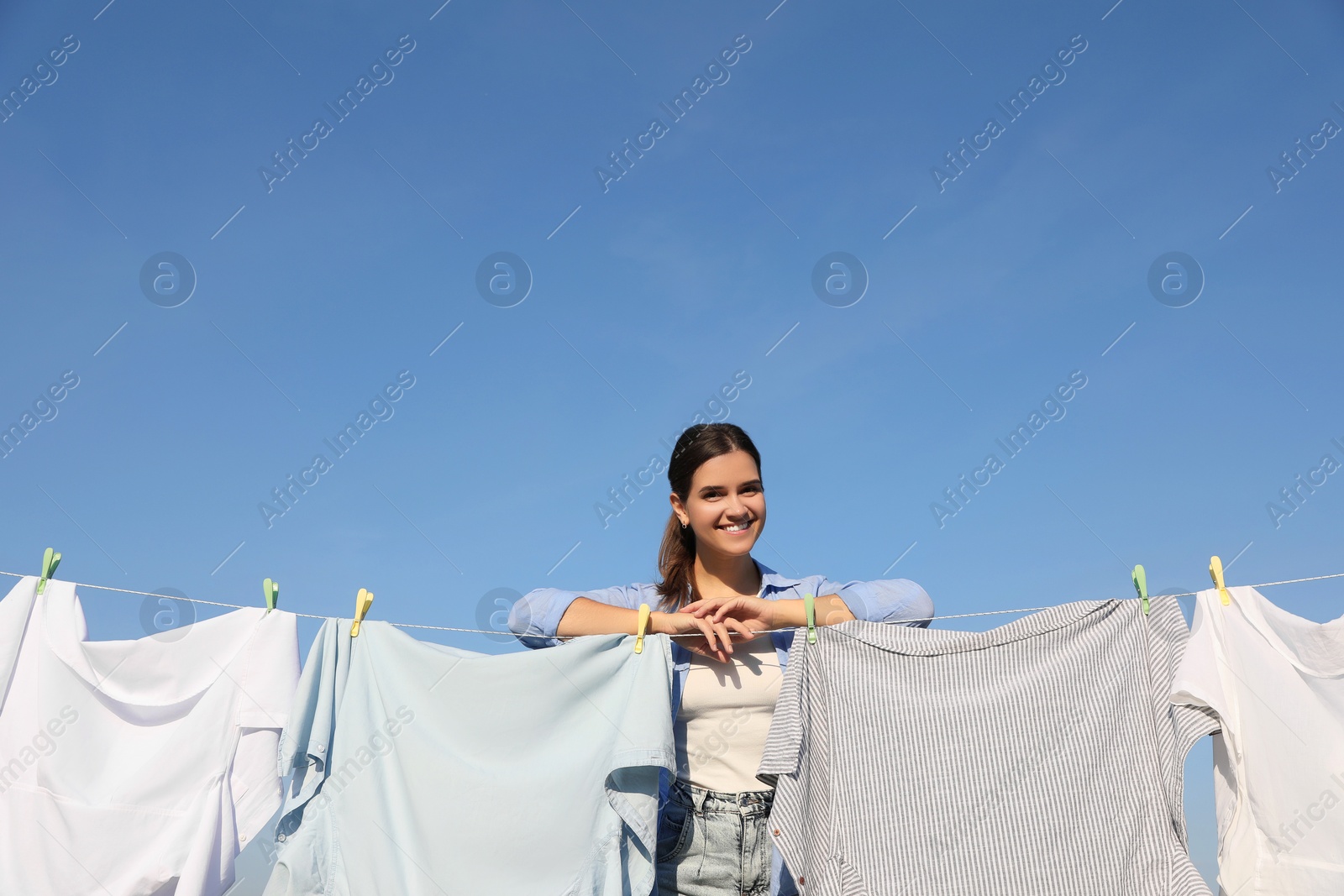 Photo of Smiling woman near clothesline with drying clothes against blue sky