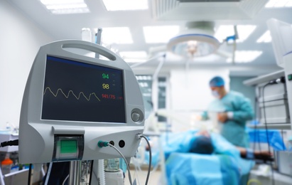 Blurred view of doctor preparing for surgery in operating room, focus on patient monitor