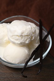 Photo of Delicious ice cream and vanilla pods in bowl on wooden table, closeup