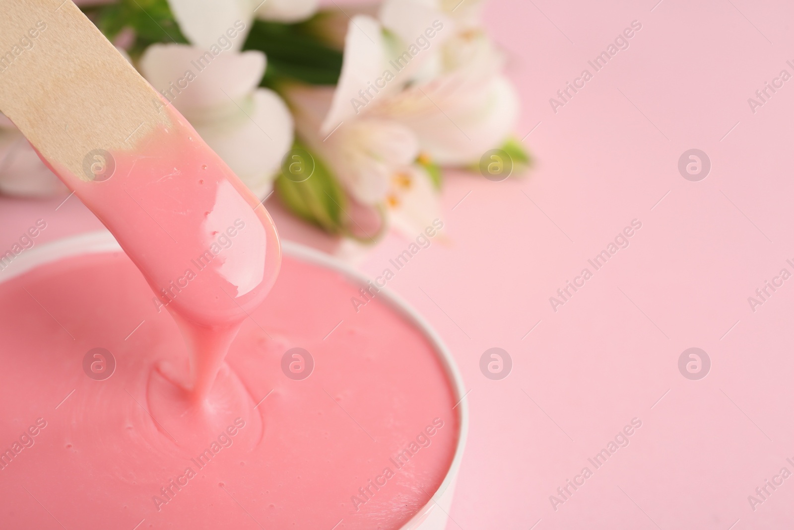 Photo of Wooden spatula and hot depilatory wax on light pink background, closeup. Space for text