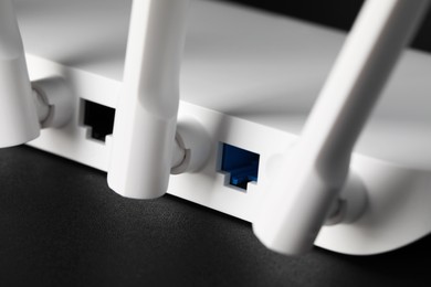 Photo of New white Wi-Fi router on black table, closeup