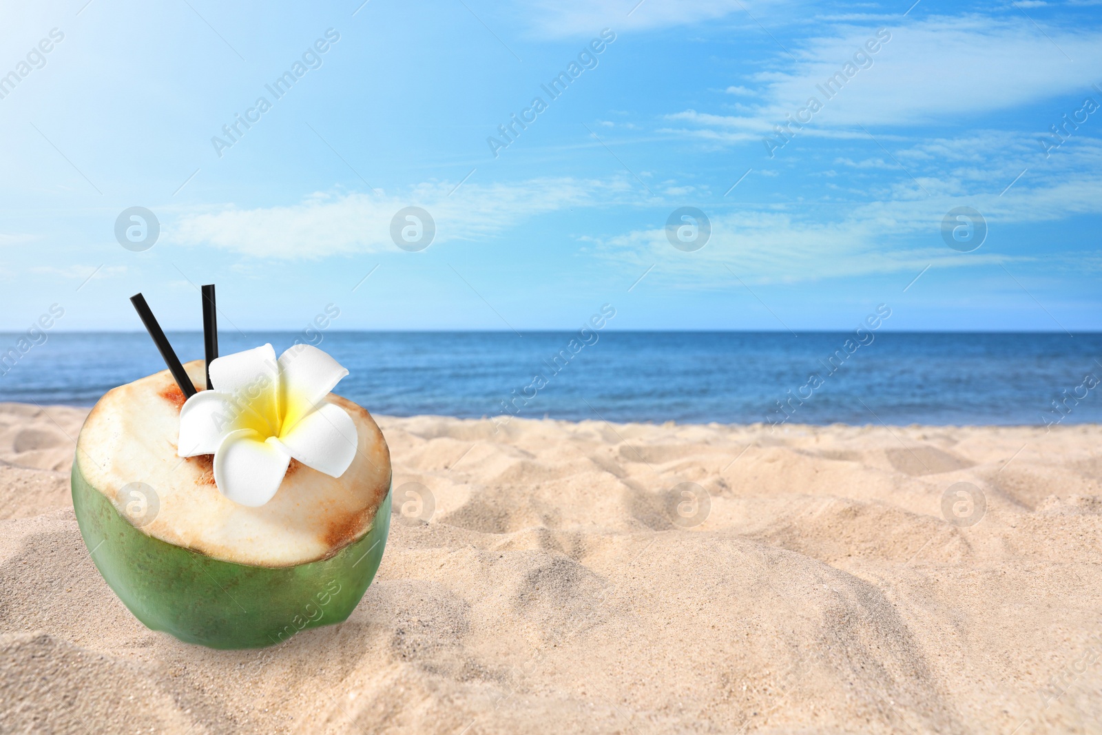 Image of Green coconut with refreshing drink and flower on sandy beach near sea, space for text