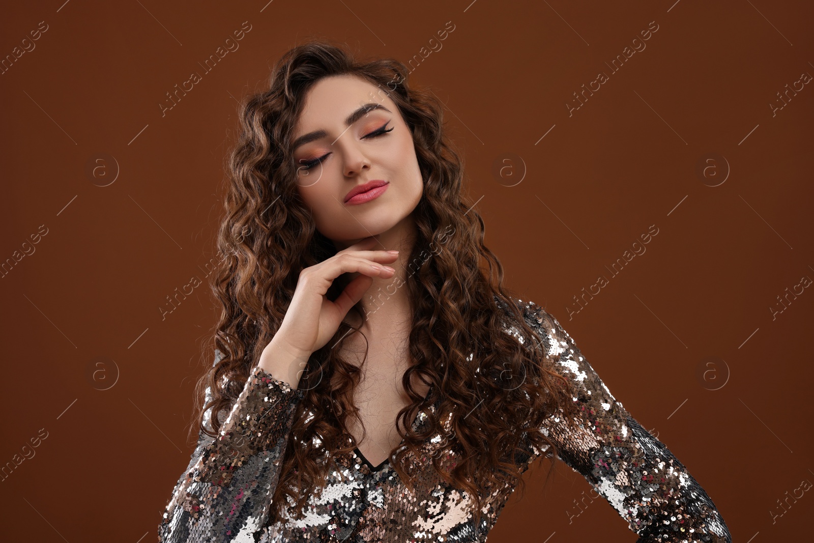 Photo of Beautiful young woman with long curly hair in sequin dress on brown background